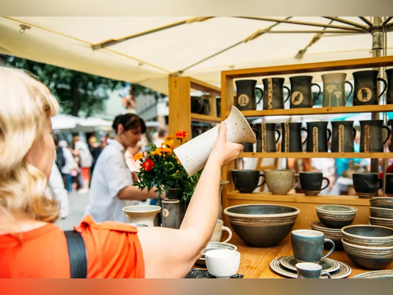 Frau schaut sich einen getöpferten Krug an einem Stand des Töpfermarkts Jena näher an.