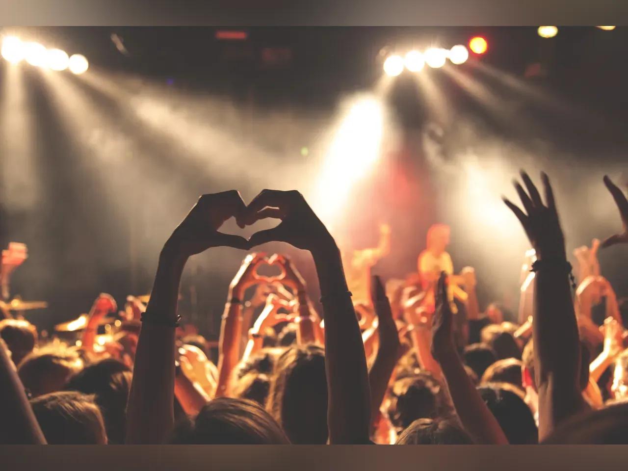 Publikum vor einer Bühne, einzelne Hände sind erhoben und zu einem Herz geschlossen