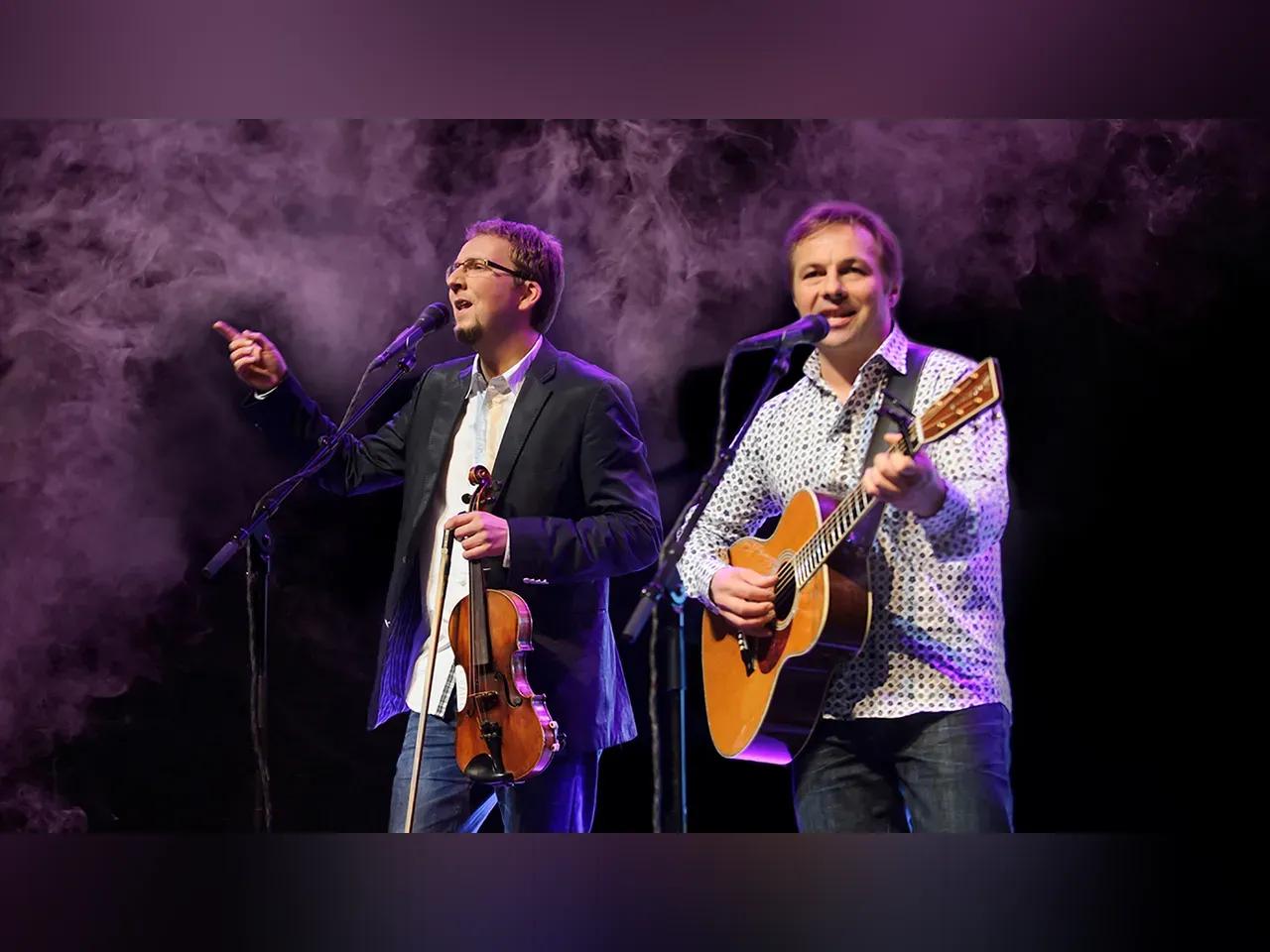 2 Musiker mit Geige, Gitarre und Mikrofonen auf einer Bühne