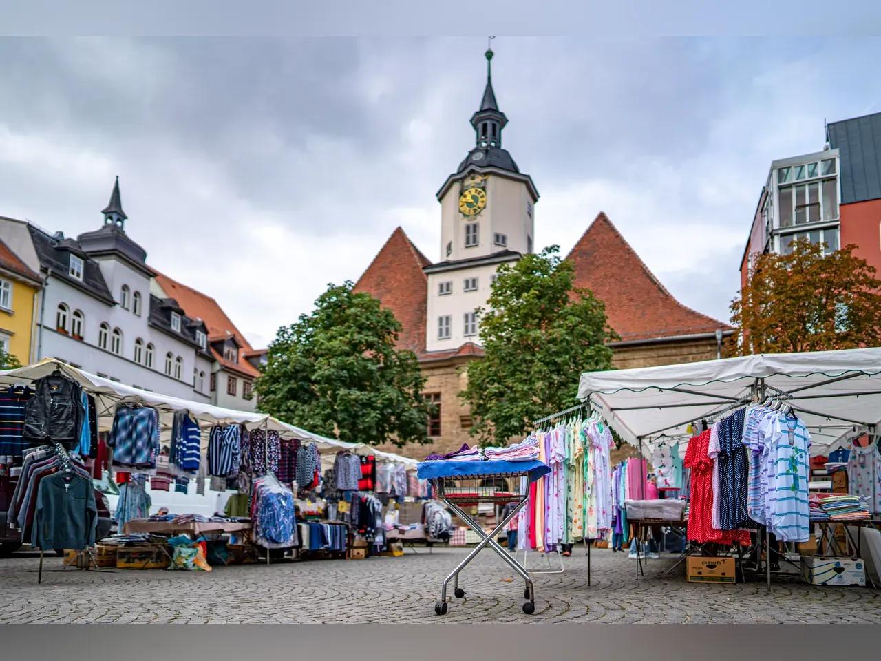 Händlerstände mit bunten Kleidungsstücken auf dem Bunten Markt in Jena stehen vor dem Jenaer Rathaus Turm.