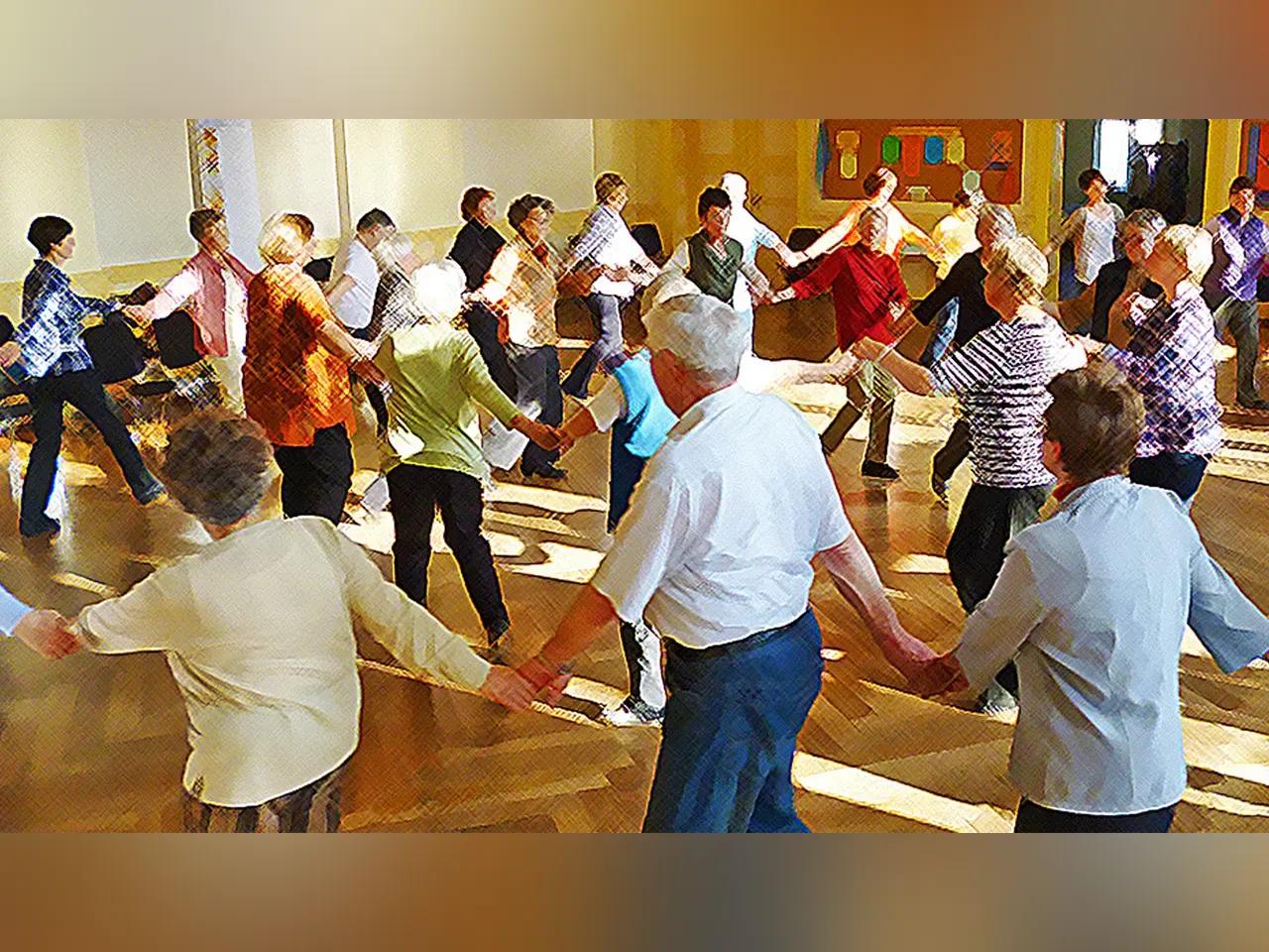 Ein Raum voller Seniorinnen und Senioren, die einen Kreistanz tanzen