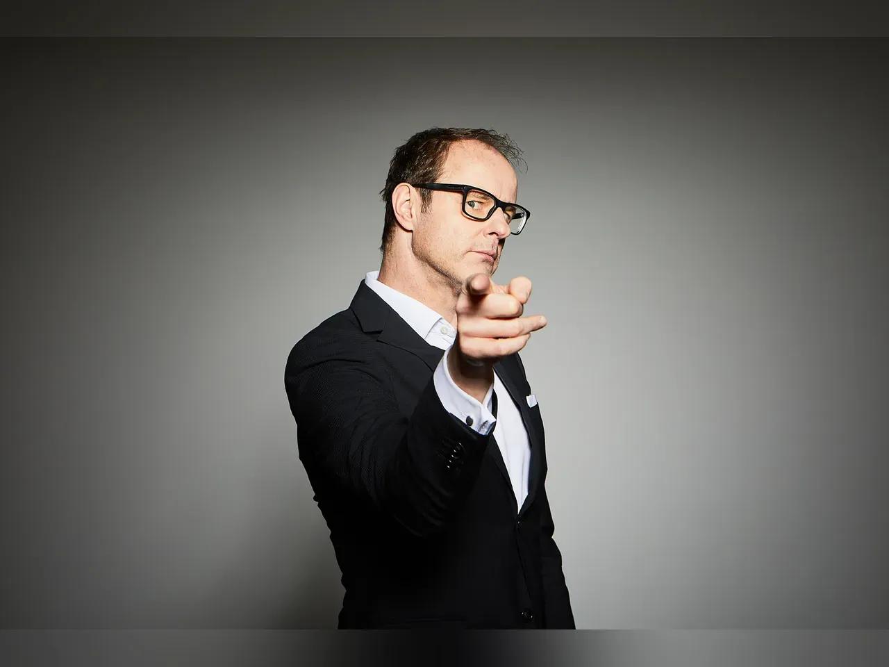 Vince Ebert in einem Anzug vor grauem Hintergrund