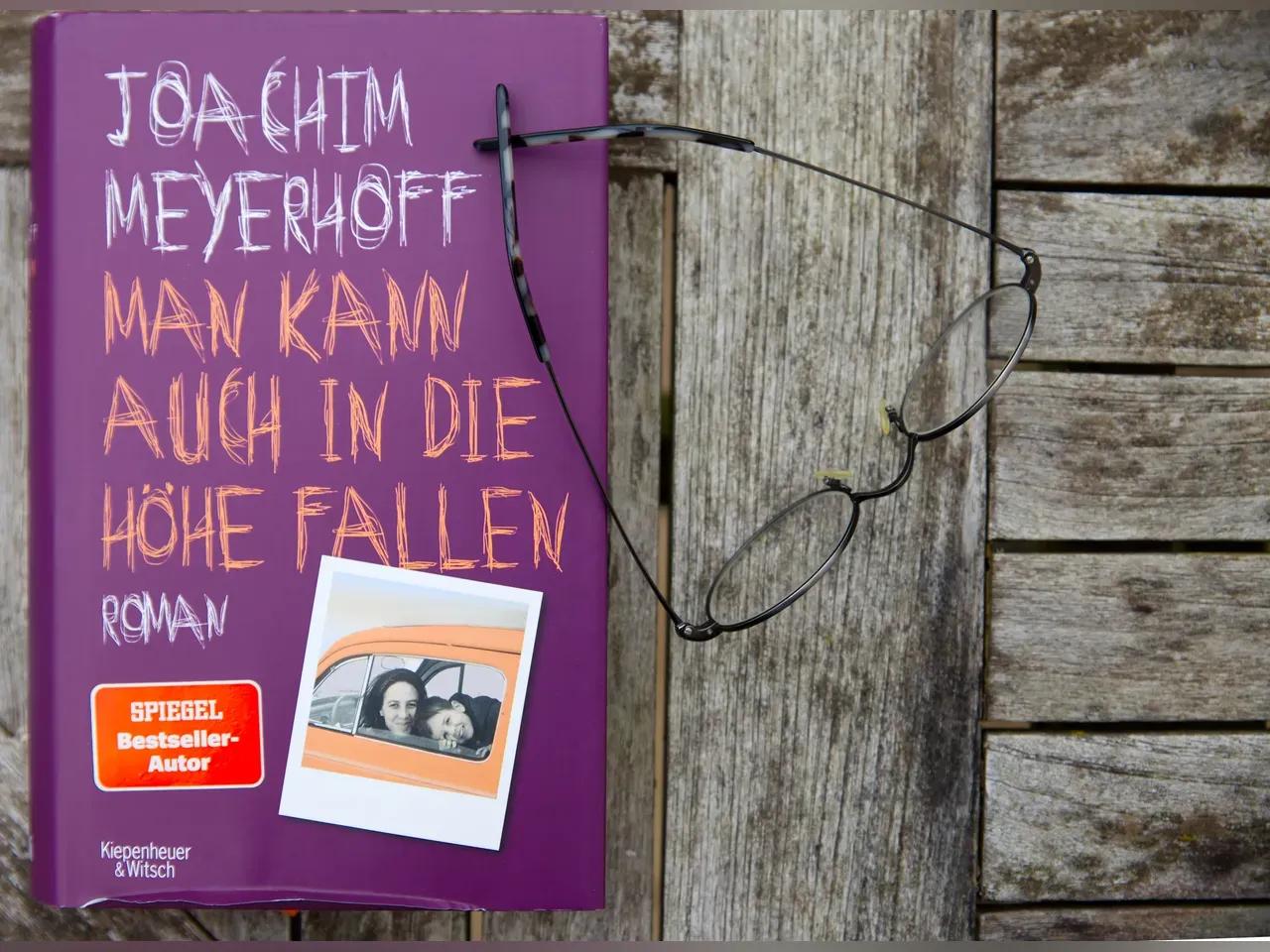 Buch "Man kann auch in die Höhe fallen" auf einem Tisch mit einer Brille daneben