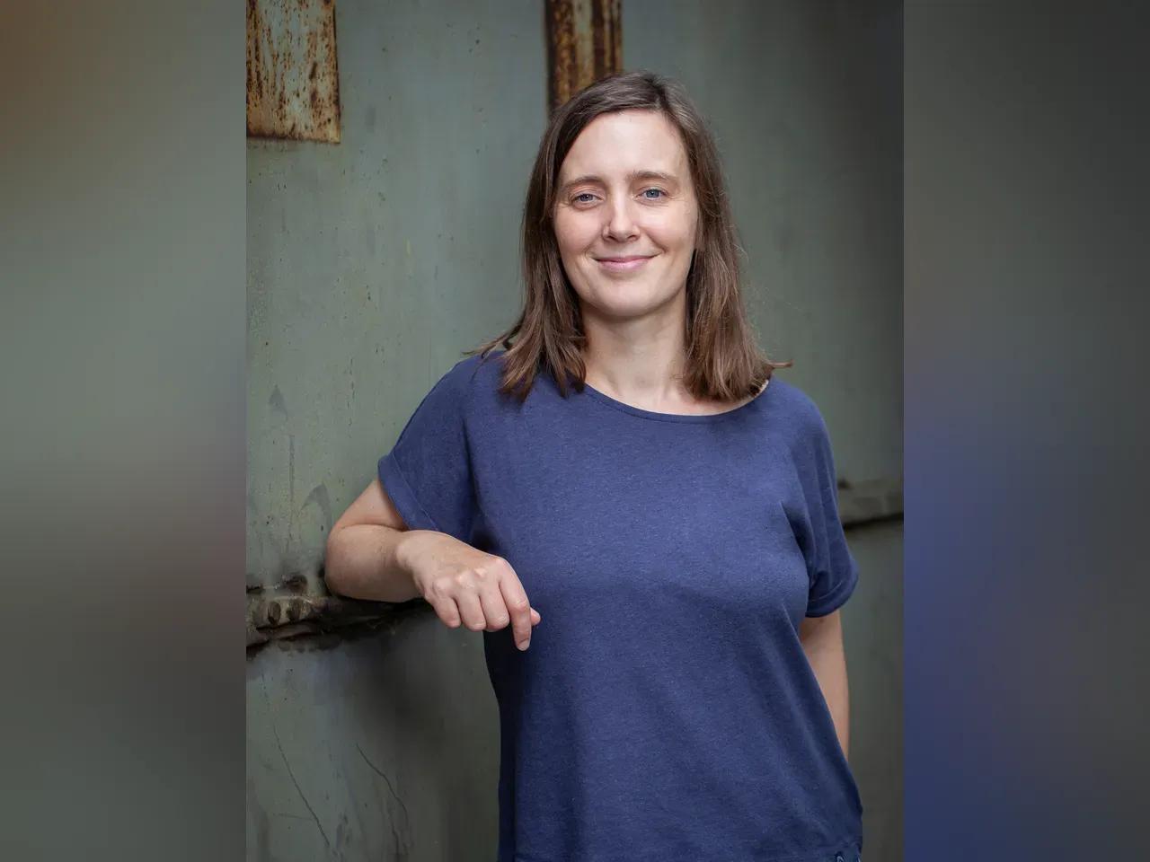 Autorin Dorothee Rise lehnt entspannt an einer Wand und lächelt in die Kamera