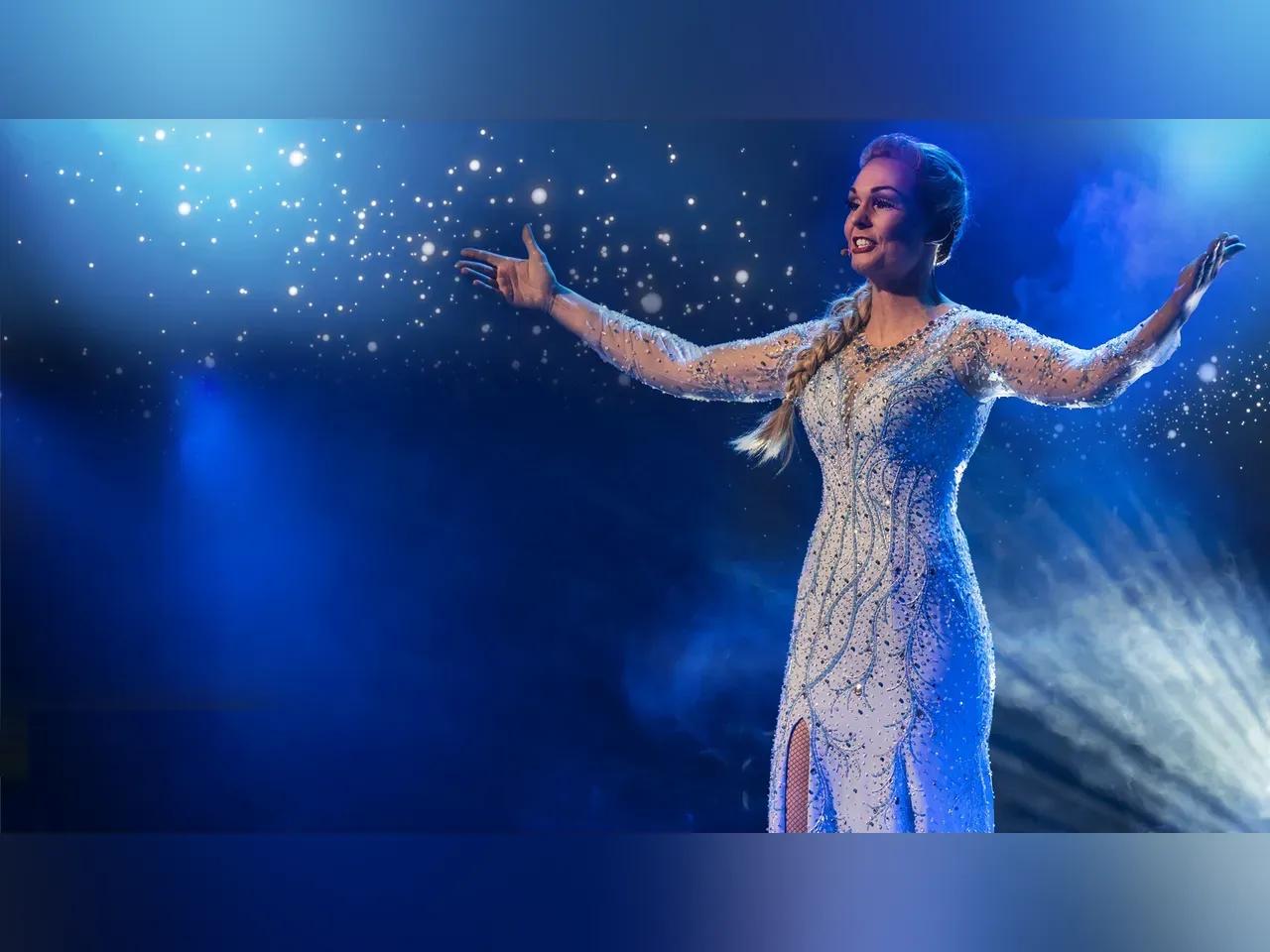 Musical-Darstellerin im "Elsa"-Kostüm steht im Rampenlicht und hat die Arme weit ausgebreitet