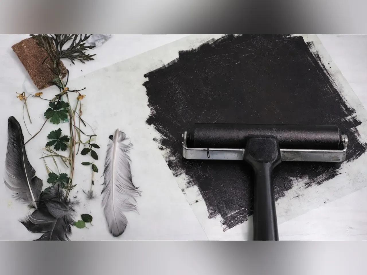Farbauftragsrolle mit schwarzer farbe, daneben Naturmaterialien wie Federn und Blätter