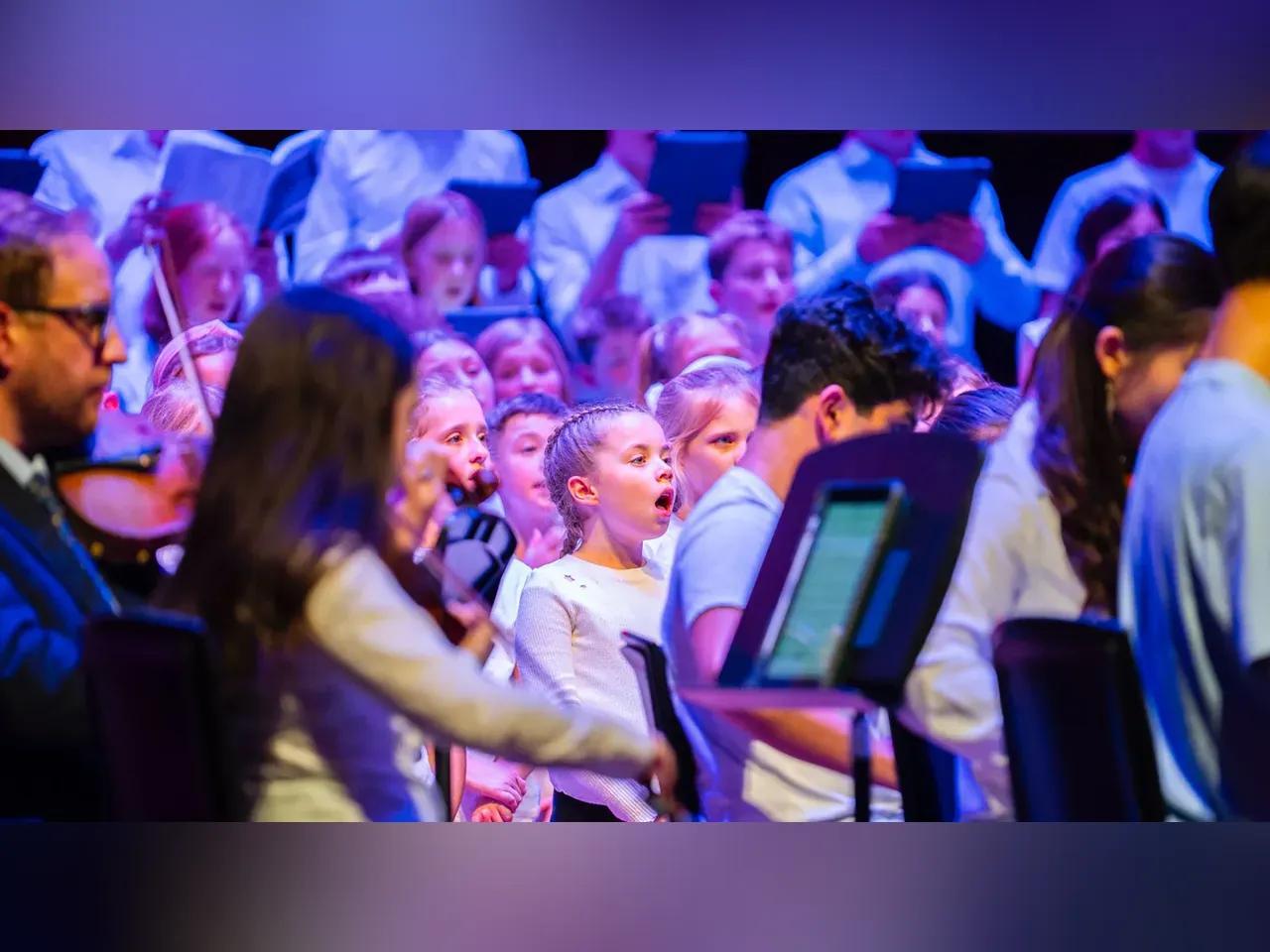 Zu sehen ist ein großer Kinderchor mit Jungen und Mädchen, die singen.