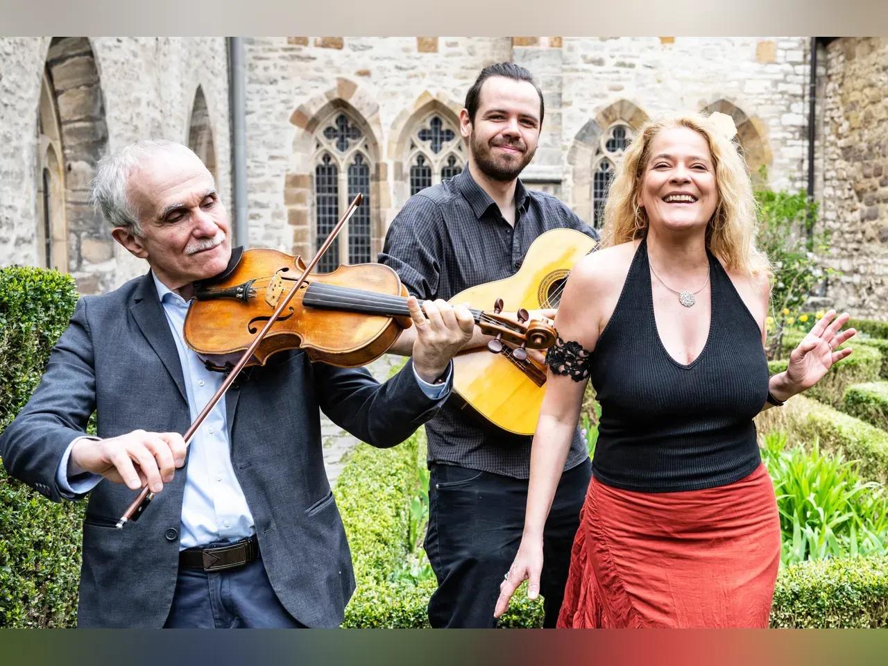 Drei Musiker:innen der Gruppe The String Company vor einem historischen Hintergrund