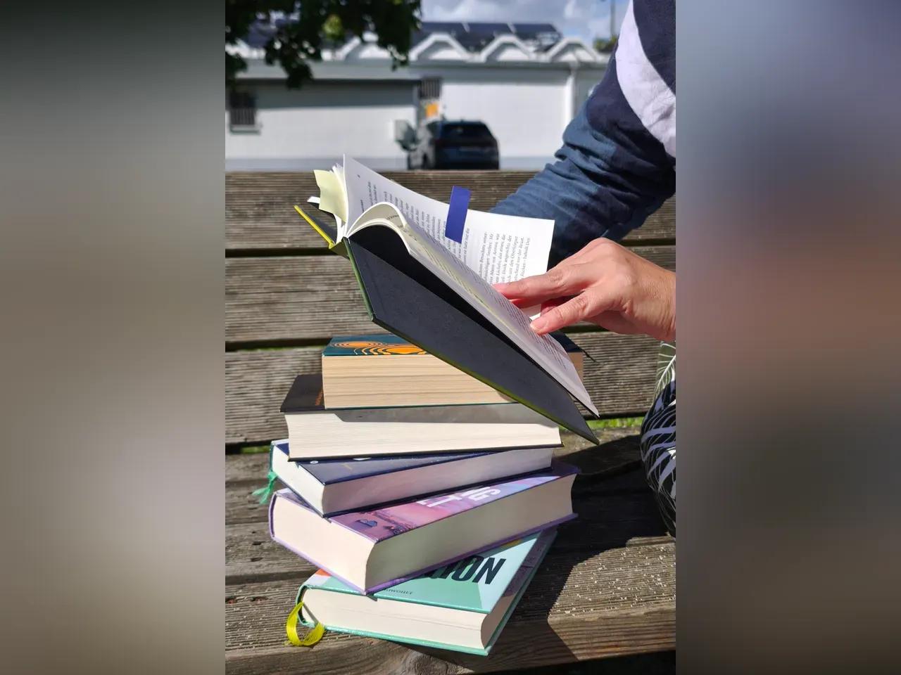 Personen blättern in einem Buch, darunter stapeln sich weitere